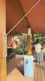 One person grills as another uses a green and white portable putting game on the patio, made of plastic and turf.