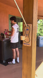 Person fills a pink bottle beside an outdoor wooden post with a Swing Putt Pro golf game set attached.