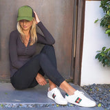 Woman in black long-sleeve top, black leggings, green trucker hat, and white sneakers sitting outdoors