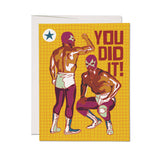 Luchador-themed greeting card featuring two masked wrestlers on a yellow grid. Printed on cardstock for celebratory occasions.