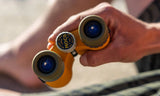 Person holding orange binoculars with a brand logo, blurred background