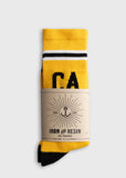 Yellow cotton crew sock with sunburst logo, brown label, and black accents, folded for display.