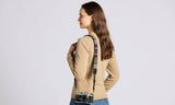 Woman wearing a beige sweater with suspenders and a camera, on a light gray background