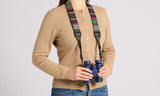 Person in tan cardigan holding blue binoculars with woven tapestry strap, set against a plain background.