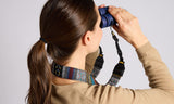 Person using binoculars with a colorful strap on a plain background