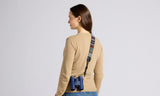 Woman wearing a beige sweater with a colorful bag strap over her shoulder on a light gray background