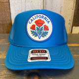 Turquoise blue high crown trucker hat with mesh back and poppy flower patch on front. Suitable for casual outdoor wear.