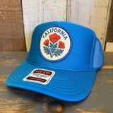 Turquoise blue high crown trucker hat with mesh back, displayed on wooden surface against a rustic background.