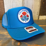 Turquoise blue high crown trucker hat with mesh back, displayed on a wooden surface.