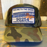 Camo winter cap in forest pattern with embroidered Take Me to the Shore 90254 patch, suitable for cold weather.