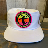White cotton baseball cap on a wooden surface, designed for beach or casual wear.