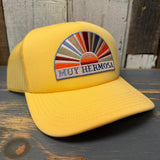 Sunset yellow foam trucker cap with embroidered MUY HERMOSA text and a sunset motif patch on the front.