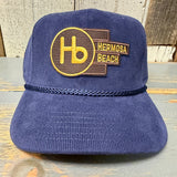 Navy blue corduroy mid-profile cap with yellow Hb patch, displayed on wood. Ideal for casual wear.