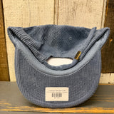 Slate blue corduroy cap with a brand label on a wooden surface