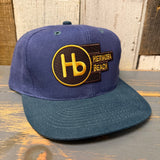 Navy and dark green 6-panel low profile cap with yellow Hb logo and front text, suitable for casual wear.