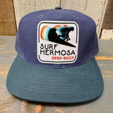 Navy and dark green 6-panel cap with a surfer patch, suitable for everyday wear.