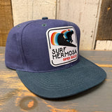 Navy and dark green 6-panel cotton cap with surfer patch, adjustable fit, casual outdoor style.