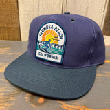 Navy and dark green 6-panel cotton cap featuring a patch with surfer, waves, pier, and sunset scene. Ideal for everyday wear.