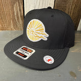 Black snapback hat with yellow sunburst HB embroidery on wood background