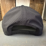 Back of black perforated snapback hat with adjustable closure on rustic wood surface