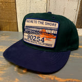 Dark green and navy six-panel cap with a fabric patch featuring Take Me to the Shore 90254 and pier graphic.