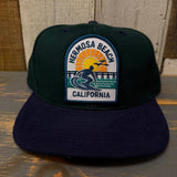 Dark green/navy 6-panel cotton canvas cap with sunset surfer patch, ideal for casual outdoor wear.