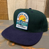 Dark green and navy 6-panel cap with a sun, surfer, and pier patch; suitable for casual outdoor wear.