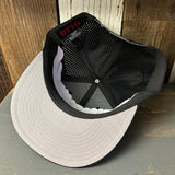 Inside view of a black mesh trucker hat with gray flat bill on wood surface