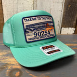 Cactus green trucker hat with white mesh panels on a wooden surface. Casual style suitable for outdoor wear.