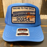 High crown blue trucker hat with a patch and 'OTTO' branding on a wooden surface.