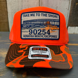 Neon orange trucker hat with a patch and branding on a wooden surface.