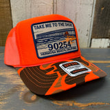 Neon orange and brown camo trucker hat with a patch on a wooden surface