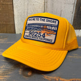 Gold trucker hat with a "take me to the shore" patch on a wooden surface