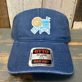 Navy cotton dad hat with lifeguard tower patch and OTTO sticker on brim, displayed on a wooden surface.