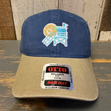 Navy and khaki dad hat with lifeguard tower and sun embroidery, made of cotton, rests on a wooden surface.