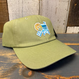 Desert green dad hat with lifeguard tower design, cotton material, displayed on a wooden surface.