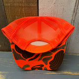Upside-down neon orange camouflage mesh cap on a wooden surface.