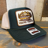Green trucker hat with 'You're Trippin'' patch on a wooden surface.