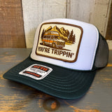 White trucker hat with green bill and a 'You're Trippin'' design and Otto logo on a wooden surface.
