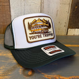 White trucker hat with green bill and with a van and mountain design on a wooden surface