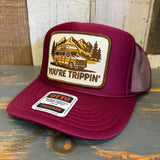 Maroon trucker hat with 'You're Trippin'' graphic and Otto logo on a wooden surface.