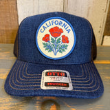 Blue trucker hat with California poppy design and Otto brand label on a wooden surface.