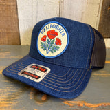 Blue denim trucker hat with California poppy design on a wooden surface.