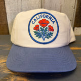 White cap with blue brim and California poppy design on a wooden surface