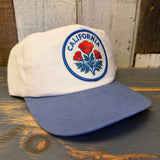 White cap with blue bill and California poppy design on a wooden surface
