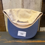 Upside-down White cap with blue bill on a wooden surface with a wooden wall background.