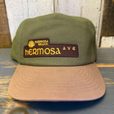 Cactus green and dune brown cap with 'Hermosa Beach Ave' patch on a wooden surface