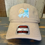 Khaki cap with embroidered lifeguard tower mini design and Otto label on a wooden surface