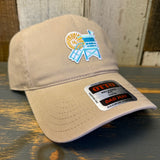 Khaki cap with embroidered lifeguard tower mini design and 'Dad Hat' label on a wooden surface