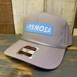 Gray cap with 'HERMOSA' patch on a wooden surface